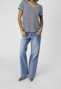 Woman wearing a black and white striped V-neck t-shirt, light blue wide-leg jeans, and blue pointed-toe heels against a plain background.