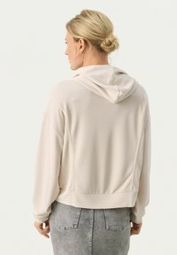Felpa leggera beige con vestibilità rilassata, dotata di cappuccio con cordino e orlo a costine. Texture liscia e design semplice senza motivi visibili.