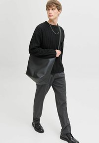 Schwarze Leder-Tote-Bag mit strukturiertem Design, matter Oberfläche und einem einzelnen Schulterriemen, kombiniert mit einem schwarzen gerippten Pullover und grauen Hosen.