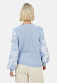 Maglione celeste lavorato a maglia con motivi a fiocco di neve bianchi sulle maniche, collo e polsini a coste, e un design dal taglio morbido.