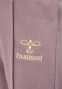 Ligblå stof med et guldbroderet logo af en bi og ordet "hummel," med en glat, tekstureret overflade.