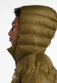 Veste rembourrée vert olive avec une texture matelassée, col haut et capuche ajustée. Comprend une fermeture éclair intégrale et un détail de logo sur la poitrine.