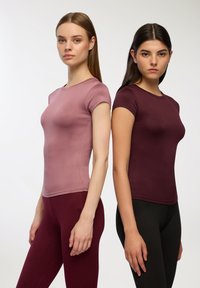 Dopasowane bluzki z krótkim rękawem w kolorze mauve i burgundowym, wykonane z gładkiego materiału z minimalnymi szwami. W komplecie z pasującymi dopasowanymi legginsami.