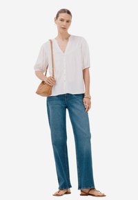 Blusa bianca con bottoni e maniche corte, abbinata a jeans azzurri a gamba larga. Gli accessori includono una borsa a tracolla beige e sandali minimalisti.