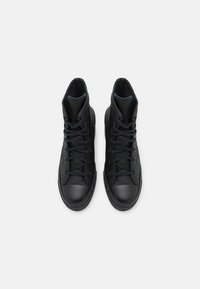 Paire de baskets montantes noires avec lacets, embouts en caoutchouc et semelles texturées, vues de dessus sur fond blanc uni.