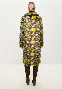 Palton cu model floral, în nuanțe de maro, verde și galben, având o textură pufoasă și un guler, asortat cu bottine maro până la genunchi.