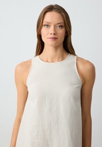 Helles beiges ärmelloses Leinenkleid mit rundem Ausschnitt und lockerer Passform. Der Stoff weist eine subtile Textur und natürliche Fasern auf.
