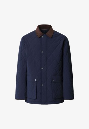 Chaqueta acolchada azul marino con un cuello de pana marrón, botones a presión y dos bolsillos frontales; textura suave con un patrón de diamante.