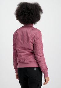 Veste bomber rose avec un col et des poignets côtelés, présentant une texture lisse et une silhouette ajustée. La vue arrière montre des détails de couture sur les épaules.