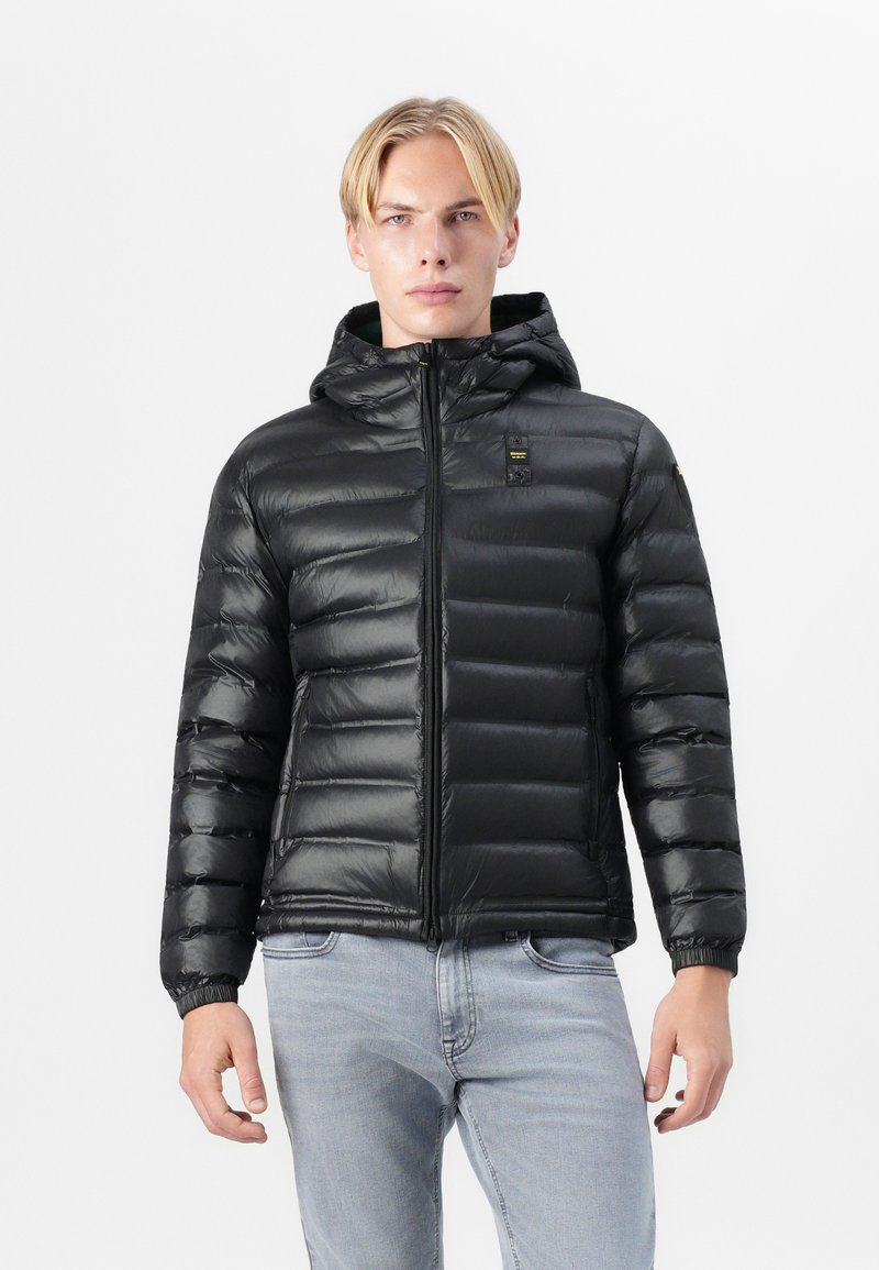 Zwarte, puffy, met dons gevulde jas met een capuchon. Voorzien van een ritssluiting, elastische manchetten en een klein logo op de borst. Glad textuur.