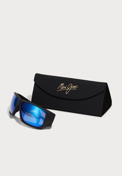Lunettes de soleil Maui Jim noires avec des verres miroir bleus, présentées dans un étui de protection noir portant un logo doré.