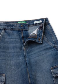 Modré džínové kalhoty s volným střihem, s zipem a knoflíkovým zapínáním. Obsahují zelenou náplň s nápisem "United Colors" a viditelné vnitřní detaily.