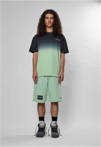 T-shirt a maniche corte con gradiente che passa dal nero al verde menta; abbinato a pantaloni corti verdi menta con etichetta. Indossato con sneakers scure.