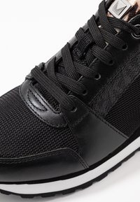 Baskets noires avec une tige texturée, des accents en cuir lisse et une semelle extérieure blanche contrastante. Les lacets sont tissés, avec des œillets en métal.