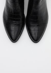 Botas negras hasta el tobillo hechas de cuero sintético texturizado de cocodrilo, con puntera afilada y suelas negras lisas.