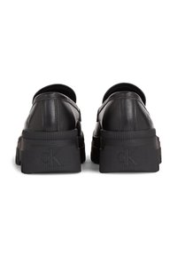 Scarpe platform in pelle nera con suola spessa, caratterizzate da una finitura liscia, dettagli di cucitura e un logo discreto sul tallone.