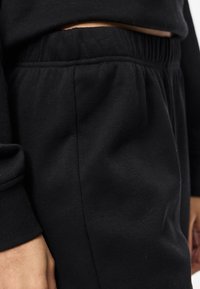 Zwarte katoenen joggingbroek met een elastische tailleband, voorzien van zijzakken en een zachte textuur. De nadruk ligt op de stof en het ontwerp van de tailleband.