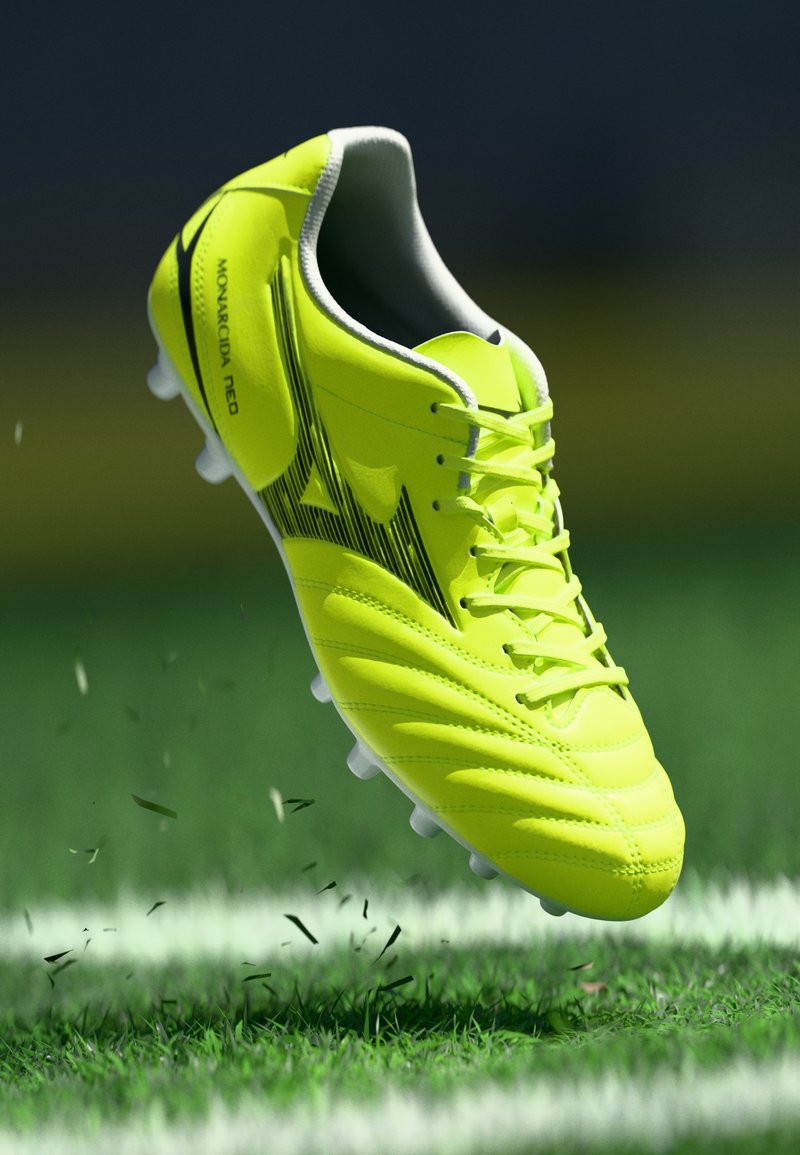 Svileni žuti nogometni kopački s crnim logotipom i vezicama, koji diže travu na zelenom terenu blizu bijele linije.