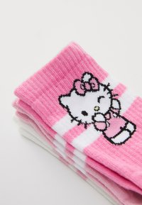Barnstrumpor med ett rosa och vitt randigt mönster. Materialet är mjukt stickat med en Hello Kitty-grafik i svart och rosa.