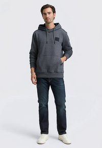 Dunkelgrauer Kapuzenpullover mit Kängurutasche und strukturiertem Stoff. Kombiniert mit dunkler Jeans und weißen Turnschuhen.