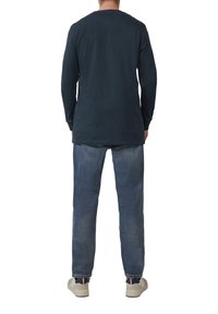 Marineblauwe longsleeve shirt, comfortabele pasvorm, zachte stof. Gecombineerd met lichtblauwe rechte jeans en crèmekleurige sneakers met contrasterende accenten.