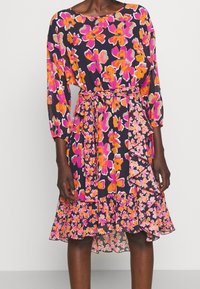 Vestido floral en azul marino oscuro con vibrantes flores rosas y naranjas. Presenta mangas largas, un lazo en la cintura y un dobladillo con volantes en capas. Tejido ligero.