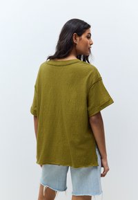 Oversized olijfgroene t-shirt met een ronde hals, opgerolde korte mouwen en een losse pasvorm, gecombineerd met licht denim shorts.