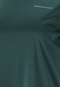 Mörkgrön idrottströja i elastiskt tyg. Har ordet "ENDURANCE" i vit text på bröstet. Slät yta, åtsittande design.