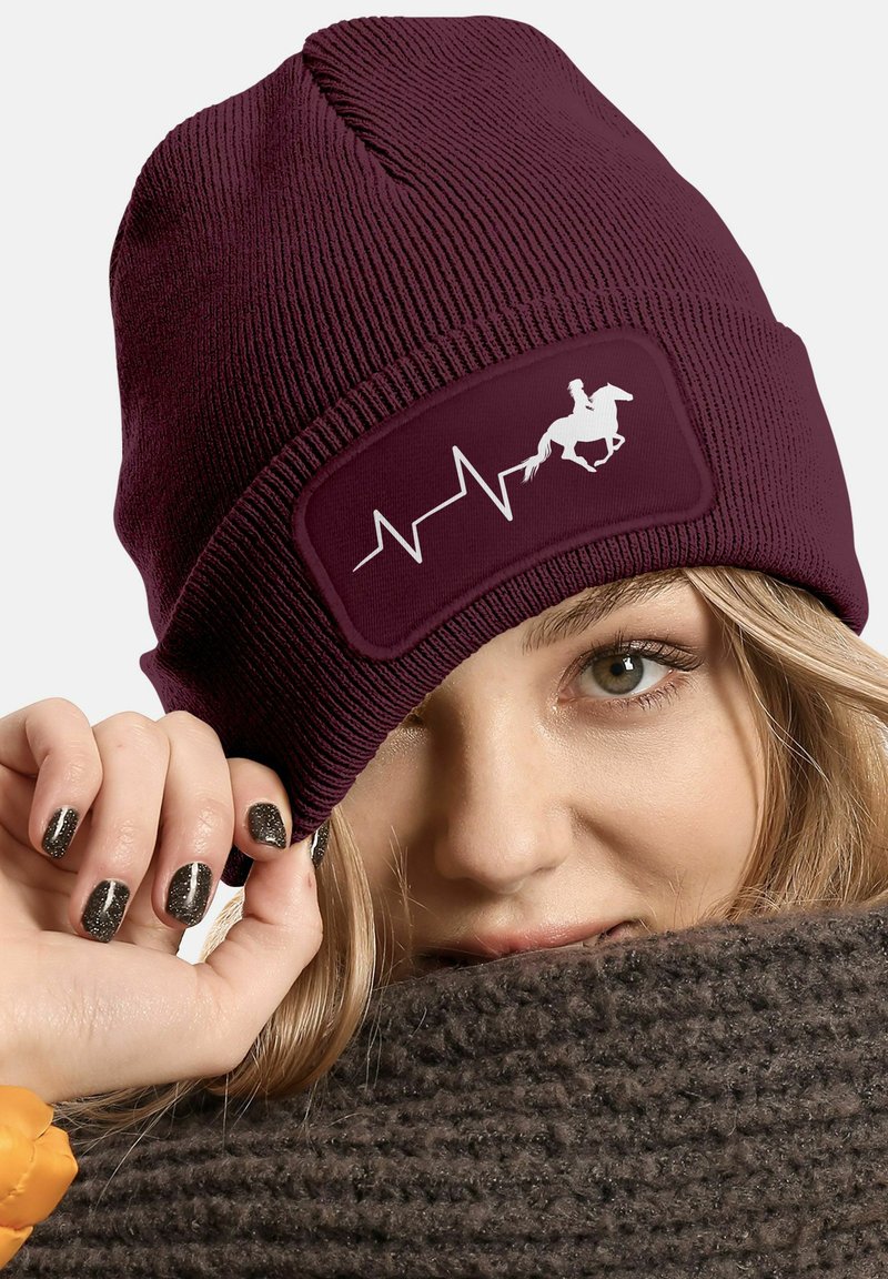 Maroon knitted beanie with a smooth fabric, featuring a rectangular patch displaying a white horse silhouette and heartbeat line design.