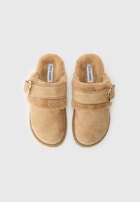 Tamne suedesne papuče s mekom podstavom i podesivim kopčama, označene s Steve Madden, prikazane na bijeloj pozadini.