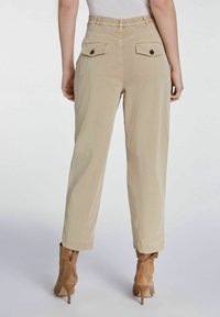 Pantalons beiges avec une coupe décontractée, dotés d'une taille élastique, de deux poches arrière avec boutons et de poignets retroussés. Tissu texturé et finition lisse.
