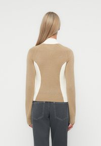 Strikkegenser med en tettsittende design med beige og kremfargede blokkeringer, ribbestrikket kant og raglanermer. Glatt tekstur, middels tykkelse.