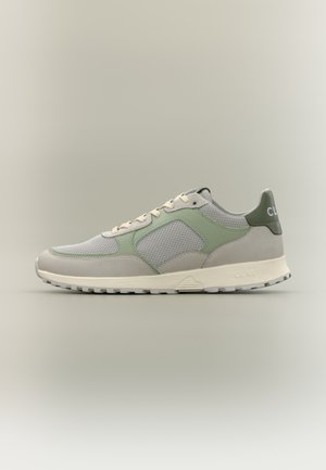 Αθλητικό παπούτσι σε ανοιχτό γκρι και πράσινο χρώμα με πάνελ από πλέγμα, μπεζ κορδόνια και λευκή σόλα, εμφανίζεται από το πλάι σε απλό ουδέτερο φόντο.