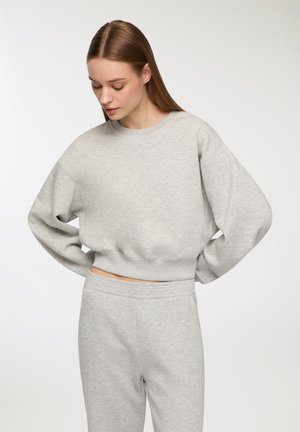Felpa grigia chiara a maniche corte con scollatura rotonda, spalle a caduta e orlo elastico. Tessuto morbido e vestibilità comoda. Pantaloni della tuta grigi abbinati.