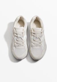 Jasnoszare sneakersy z panelami z siateczki i zamszu, z sześcioma otworami na sznurowadła i teksturowanymi podeszwami. Logo marki jest widoczne na języku.