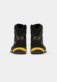 Čierne a žlté turistické topánky zobrazené zozadu, s Vibram podrážkami a vysokou podporou členku na plain bielom pozadí.