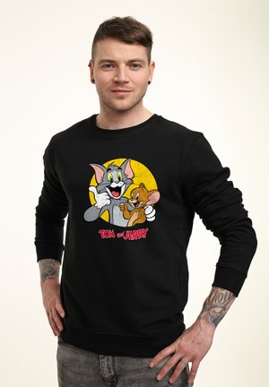 Sort sweatshirt med et farverigt grafik af Tom og Jerry, med en rund gul baggrund, lavet af blødt stof med ribbede manchetter og kant.