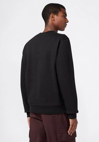 Felpa nera con scollo rotondo, maniche lunghe e polsini a coste. Presenta una texture liscia e opaca e una vestibilità comoda.