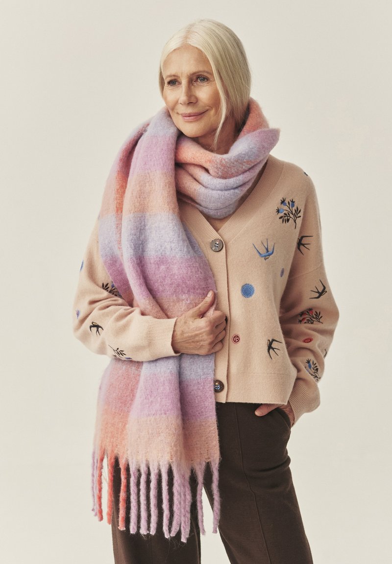 Hele roosa kootud kardigan lillemustrilise tikandi ja nuppudega, kombineeritud suure pastelltriibulise salli ning lontis servadega.