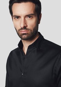 Czarna koszula z kołnierzykiem na guziki, o gładkiej fakturze i subtelnym wzorze. W wyposażeniu czarne guziki oraz dopasowany krój.