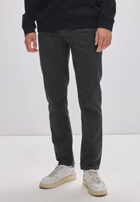 Tmavě šedé džíny se strukturovaným povrchem, slim fit a středním pasem. V páru s bílými teniskami s béžovými akcenty.