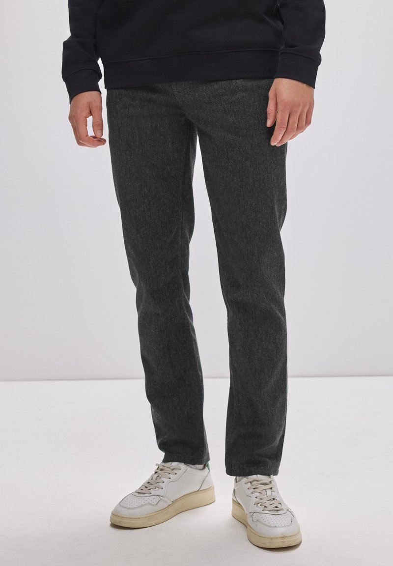 Tmavě šedé džíny se strukturovaným povrchem, slim fit a středním pasem. V páru s bílými teniskami s béžovými akcenty.