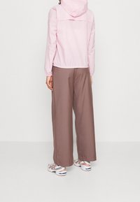 Lys pink vindjakke med hætte, elastisk talje, parret med brune vide bukser. Hvide og pink træningssko fuldender outfittet.