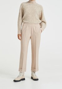 Beige neulepaita korkealla kauluksella ja löysällä leikalla, yhdistettynä vaaleanbeigeihin räätälöityihin housuihin, joissa on joustava vyötärö ja käännetyt lahkeet.