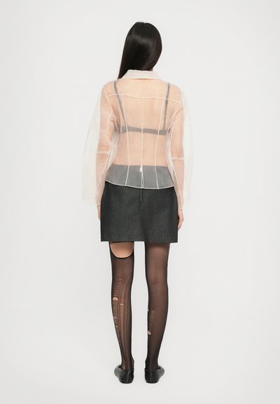 Kasutamata pikkade varrukatega läbipaistev tops, hall seelik ja mustad sukkpüksid lõike- ja tekstuuridetailidega, mida täiustavad mustad kingad.