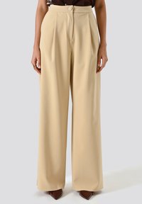 Pantaloni beige a gamba larga realizzati in tessuto morbido, caratterizzati da vita alta, pieghe e chiusura con bottone frontale.