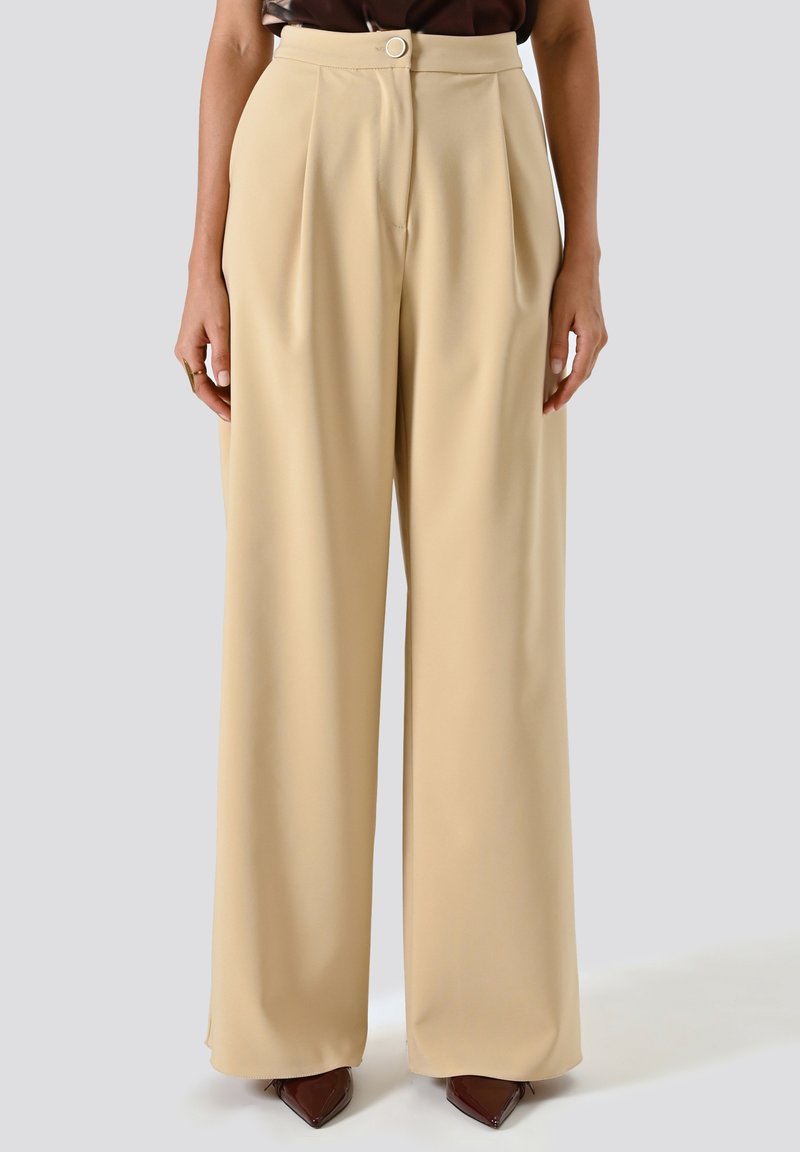 Pantaloni beige a gamba larga realizzati in tessuto morbido, caratterizzati da vita alta, pieghe e chiusura con bottone frontale.