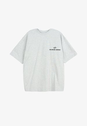 Jasnoszary, oversize T-shirt z krótkimi rękawami oraz czarnym napisem „FOLLOWING FORWARD” i symbolem na lewej piersi.