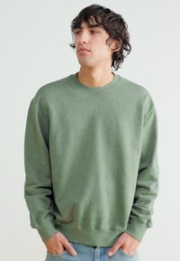 Green crewneck sweatshirt in soft cotton blend, featuring ribbed cuffs and hem, relaxed fit, and subtle texture. Simple and versatile design.