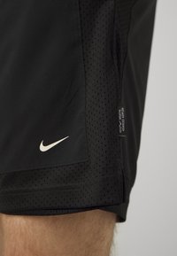 Mustad mustad Nike lühikesed püksid, millel on perforatsioonitunne, elastne vöökoht ja valge Nike logo allosas. Sildil nähtav külgõmblusel.